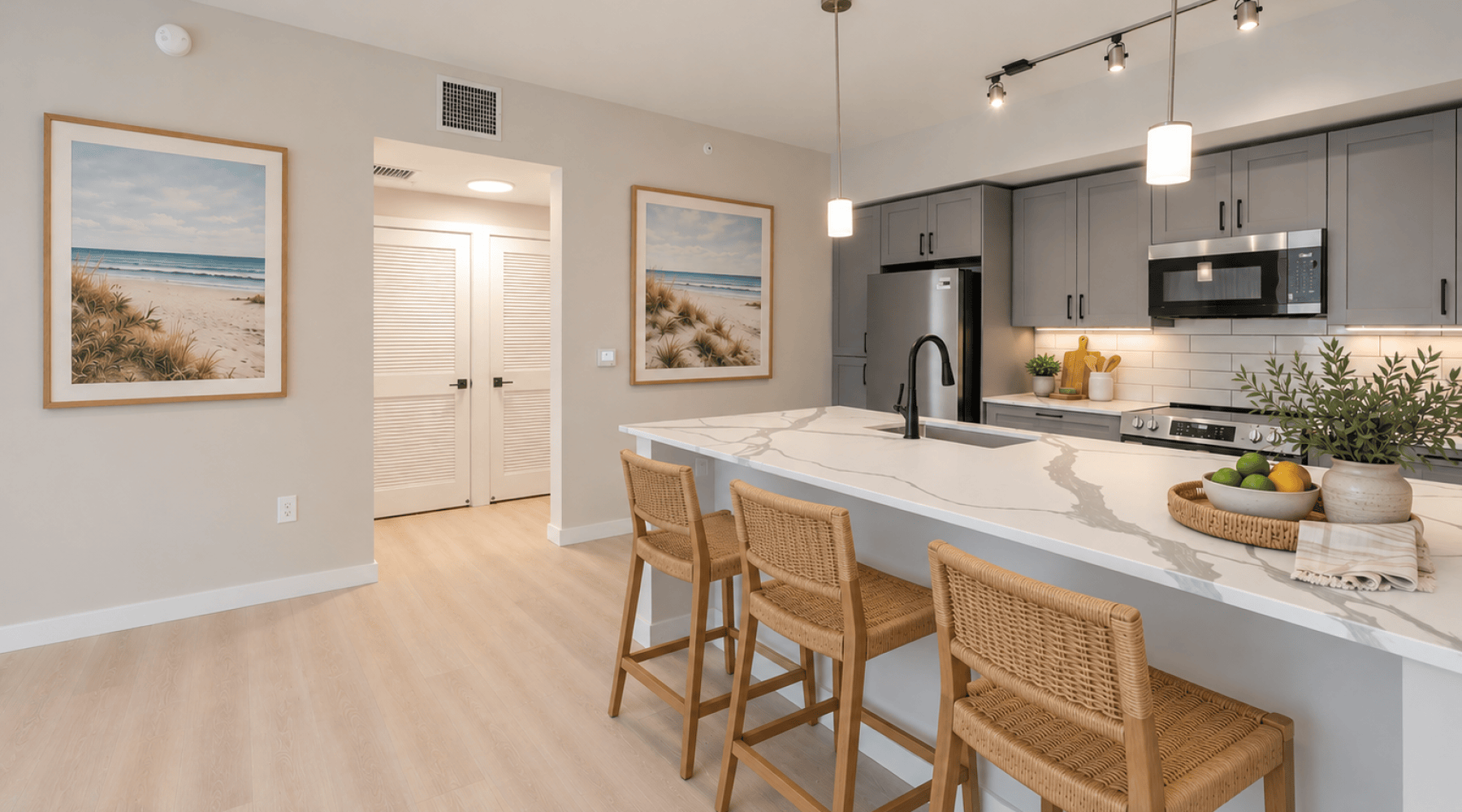 Modern kitchen at Shalimar at Boynton Beach with quartz island, woven stools, grey cabinets, and stainless steel appliances.