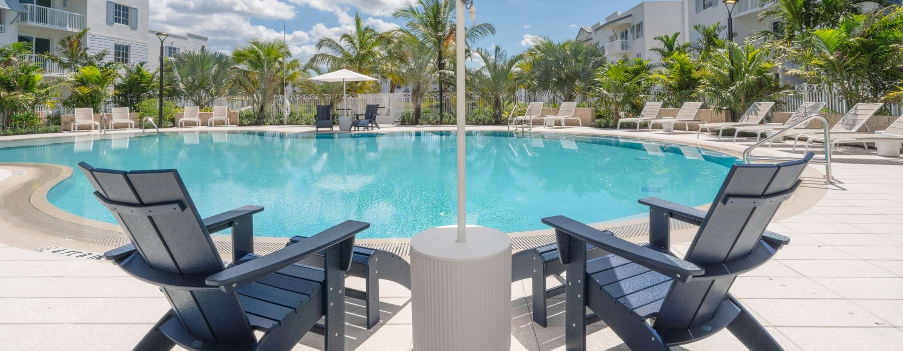 Blue lounge chairs under a white umbrella overlooking the swimming pool at Shalimar at Boynton Beach.
