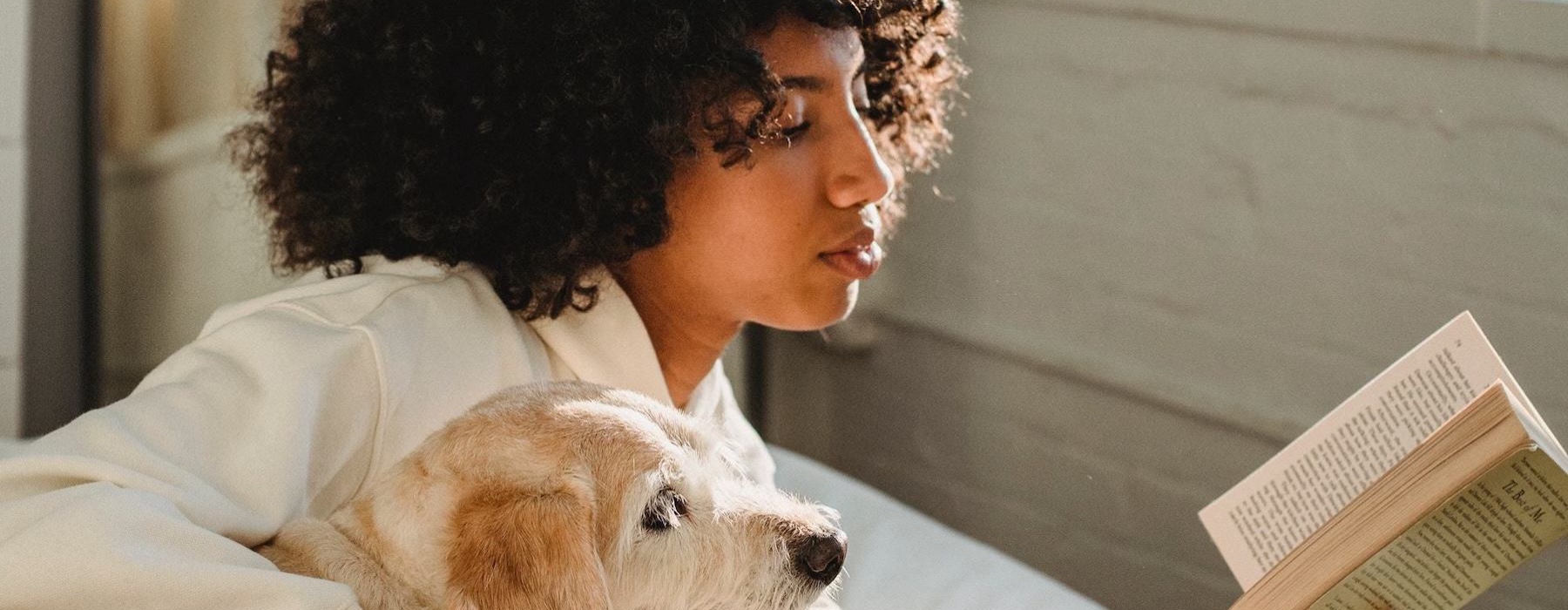 a person reading a book while laying next to a dog